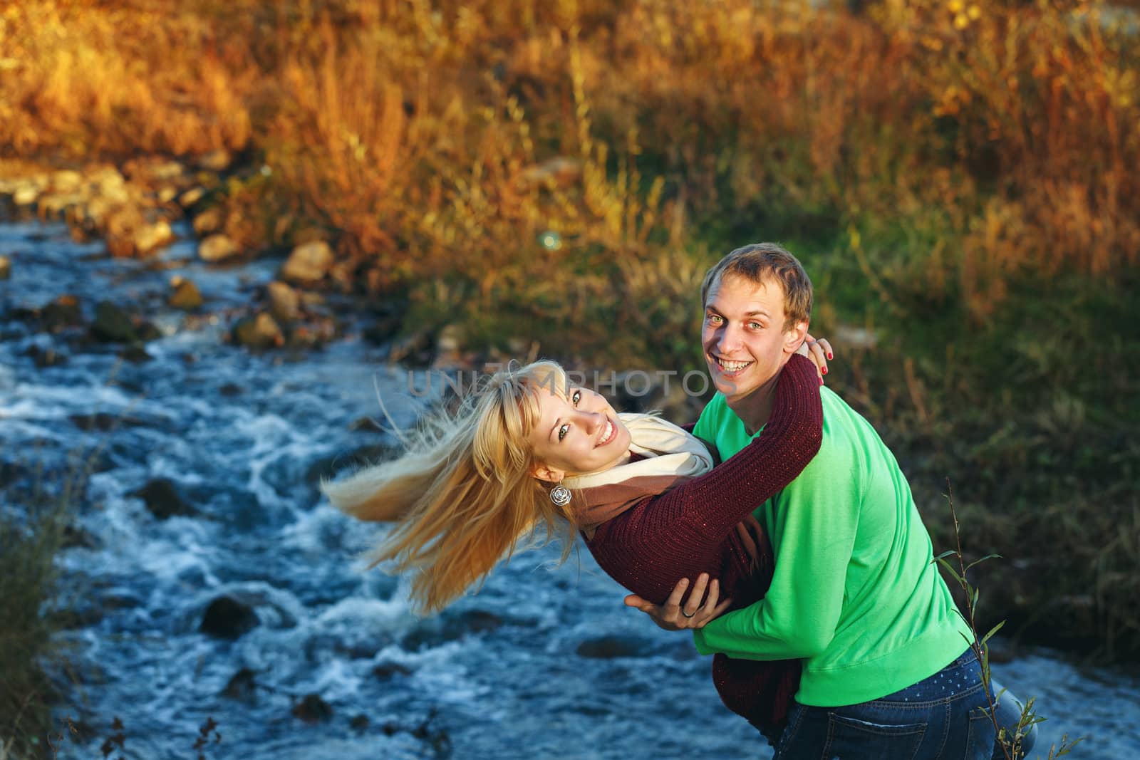 Young attractive couple embracing on the riverbank fall day