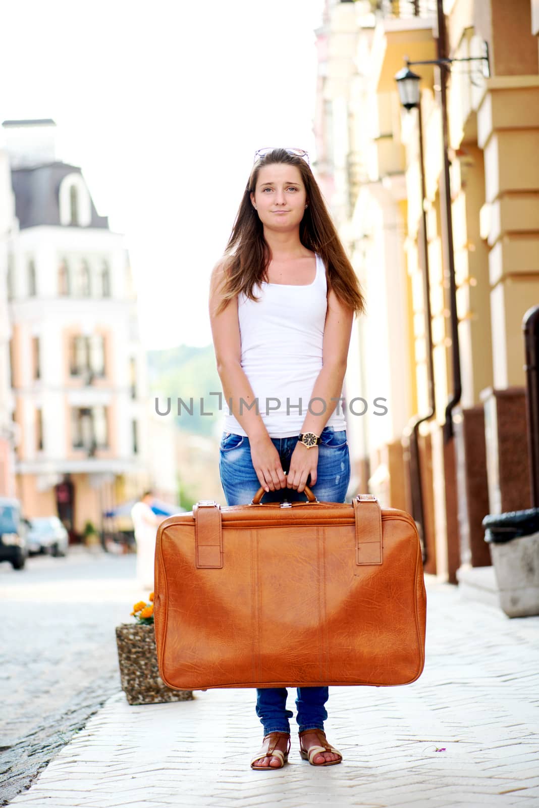 Sad looking girl with luggage in city by Nanisimova