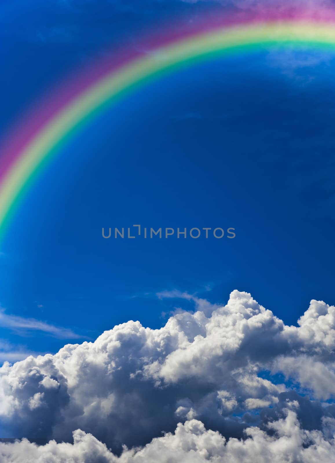 Vertical image of a blue sky with white clouds and a rainbow