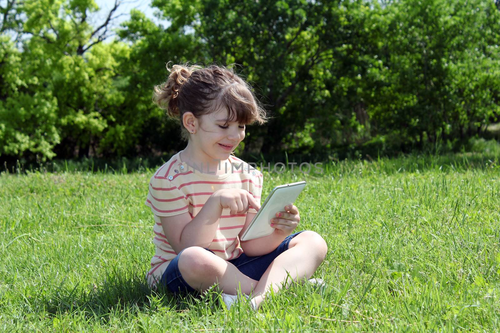 happy little girl sitting on grass and play with tablet
