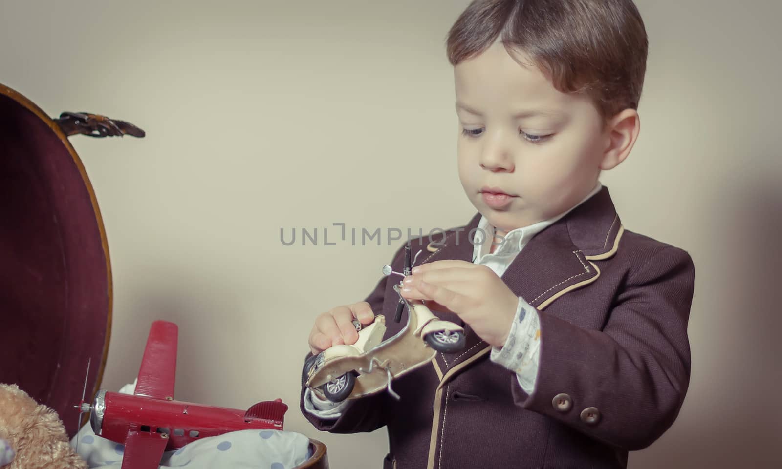 Vintage portrait of cute little boy playing with antique tin toys found in a old case. Retro style concept.