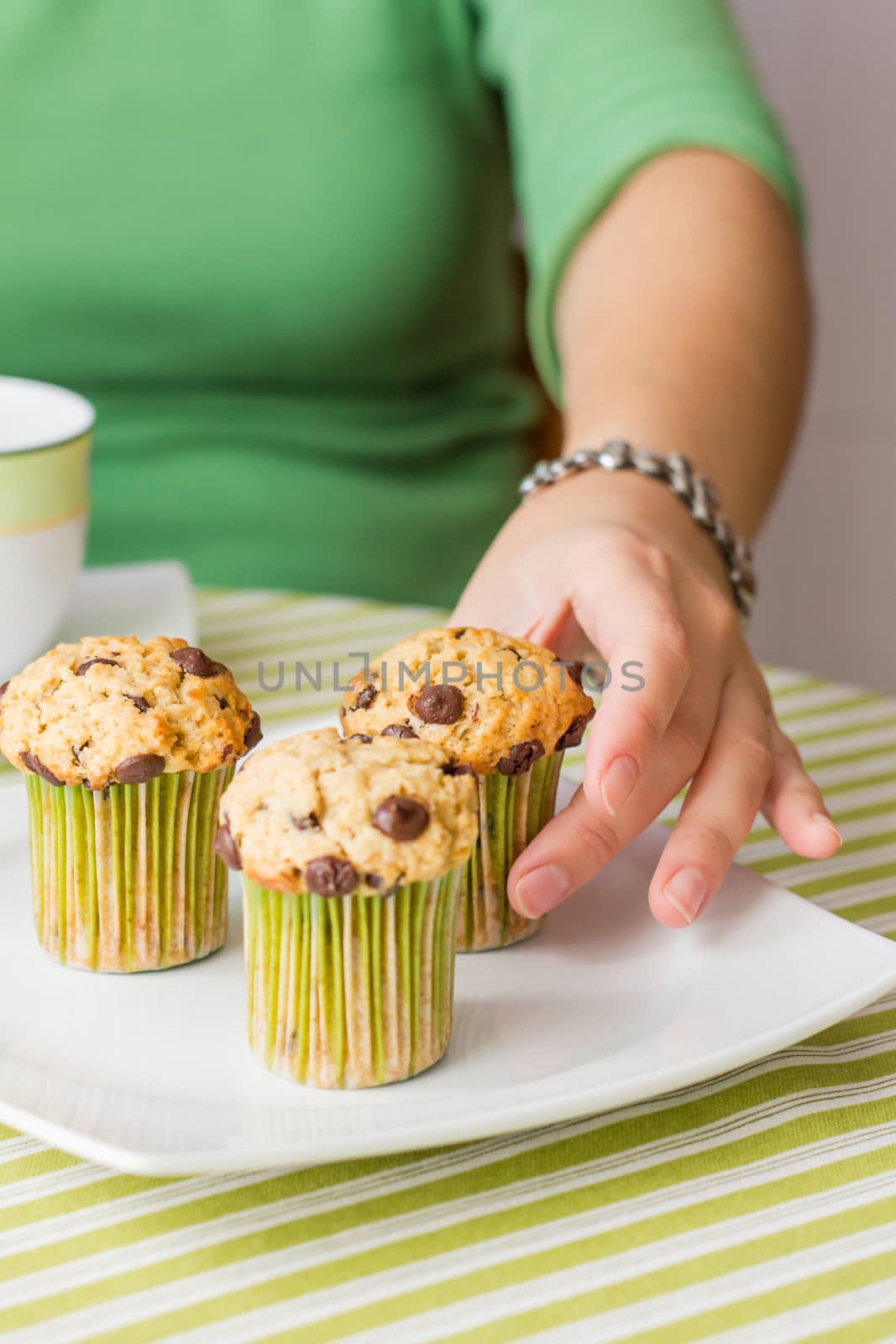 Nice girl hand taking delicious chocolate chip muffin at breakfast in green striped tablecloth