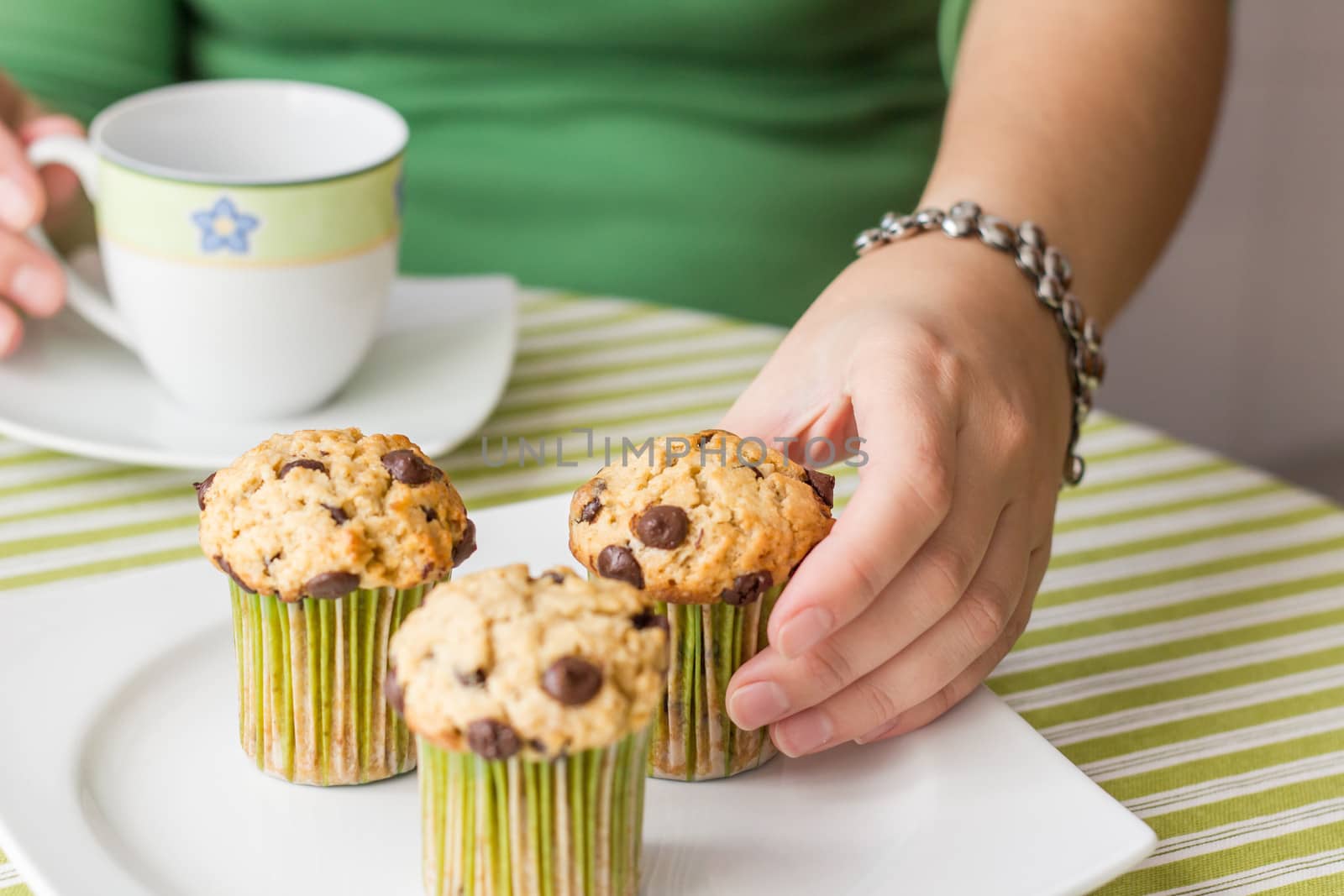 Nice girl hand taking delicious chocolate chip muffin at breakfast in green striped tablecloth