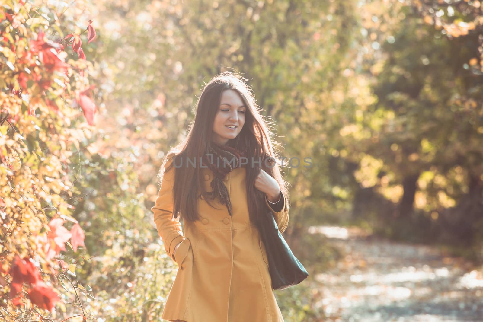 Woman is walking in autumnal park in yellow coat