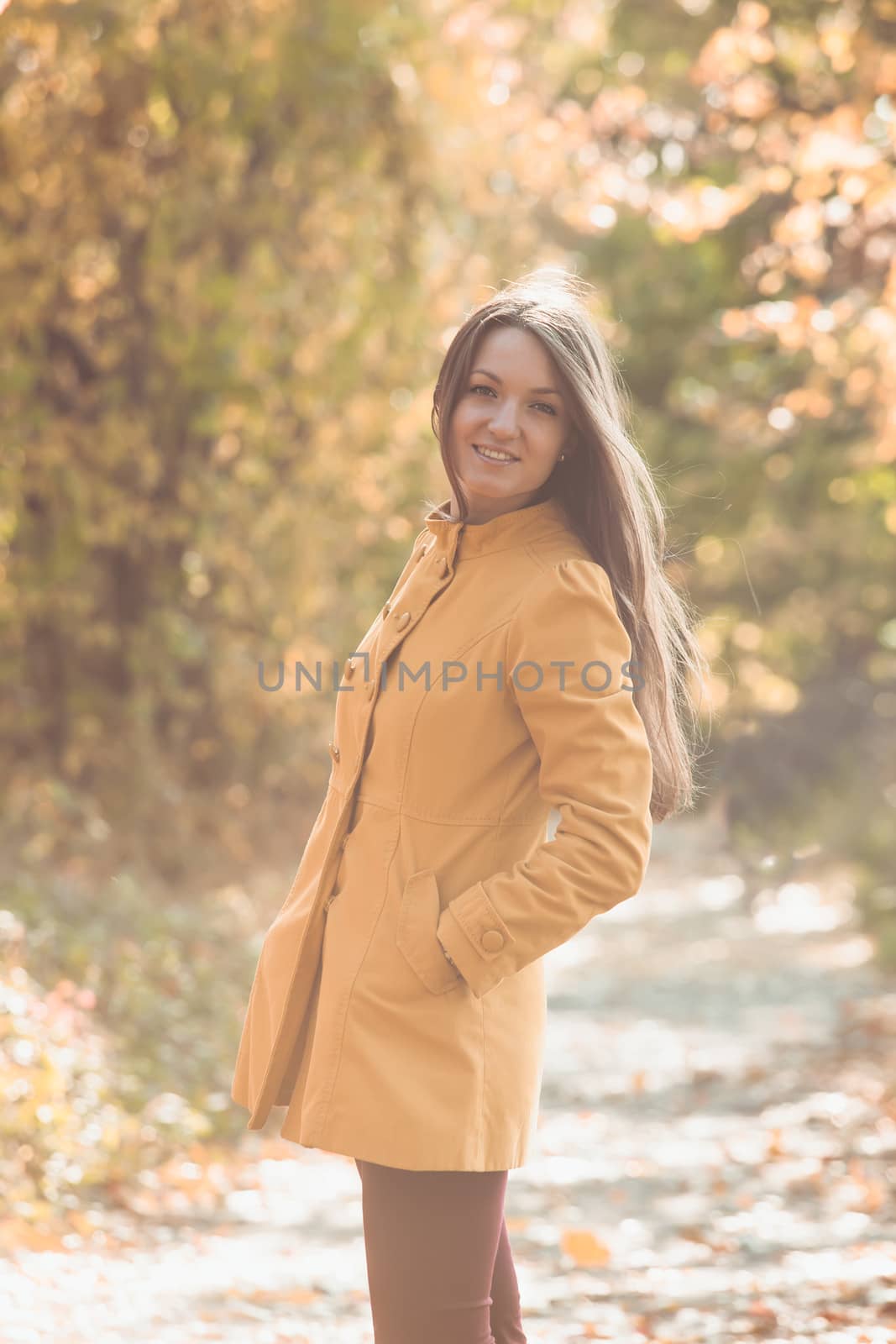 Woman is walking in autumnal park in yellow coat