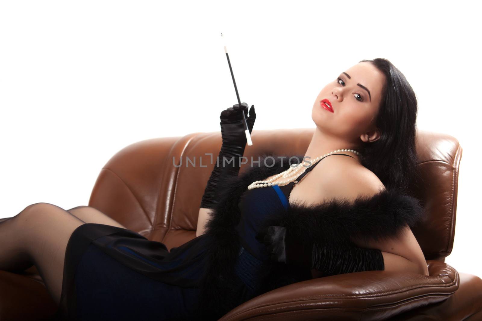 Young woman in retro clothing lying in a big chair with a cigarette holder, on white background
