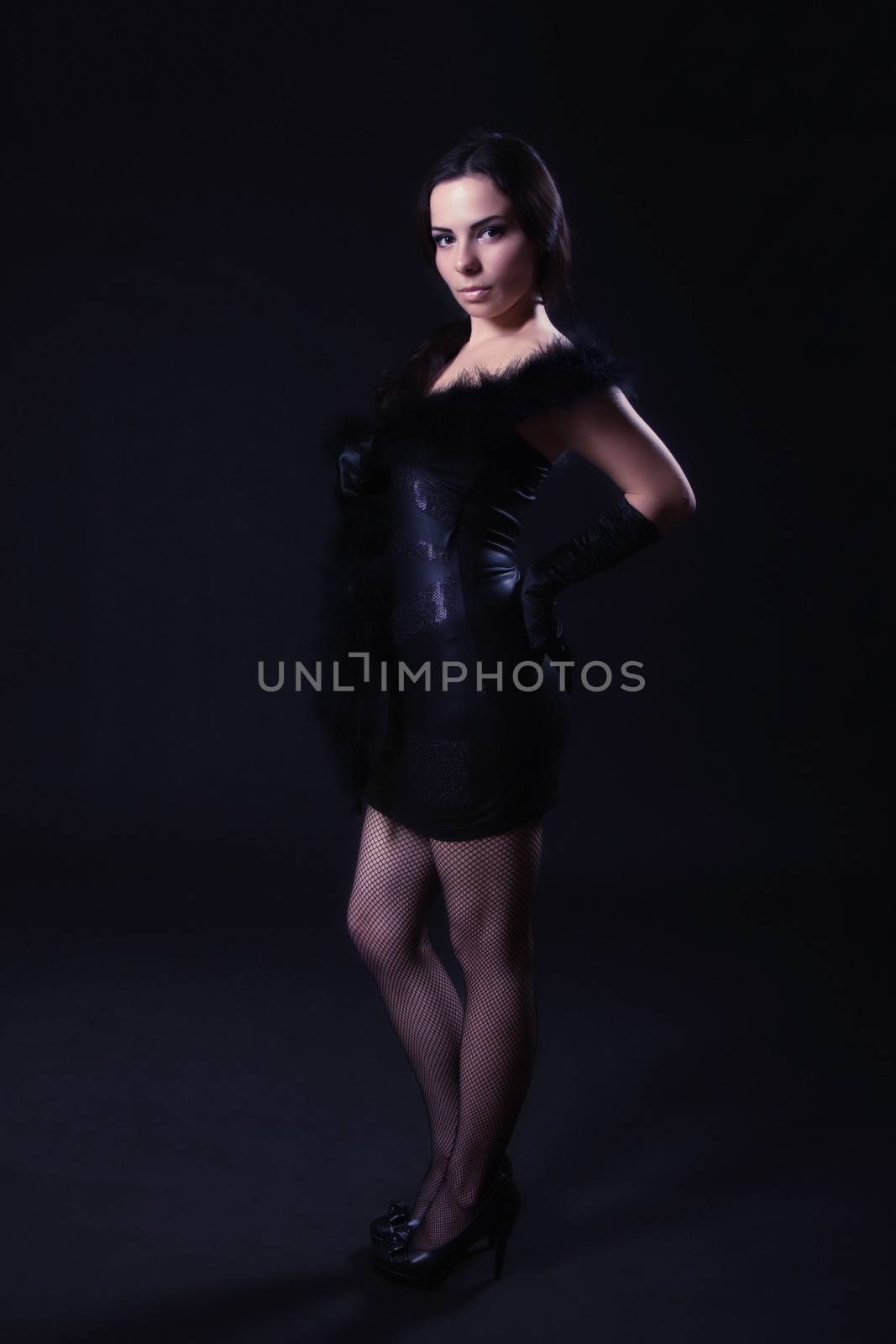 Young woman in a leather black dress posing on a dark background