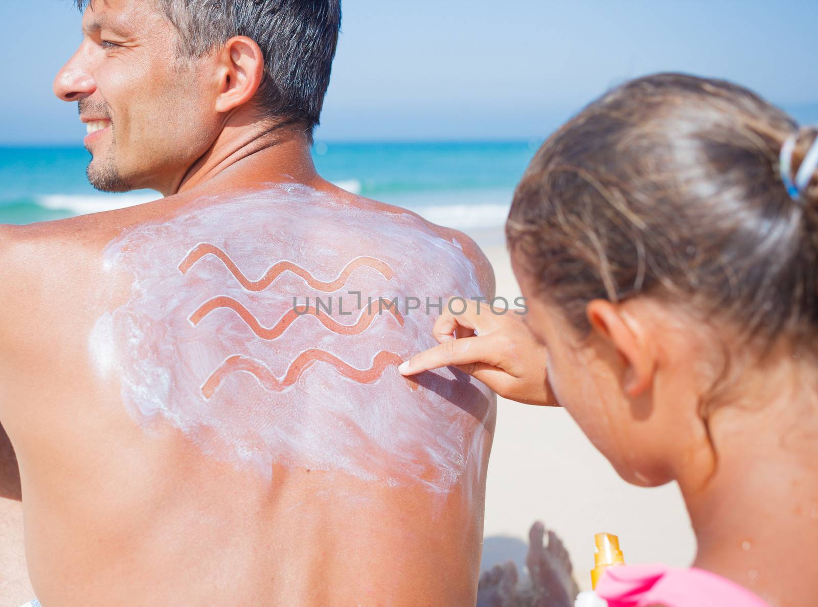 Adorable girl at tropical beach applying sunblock cream on a father's back.