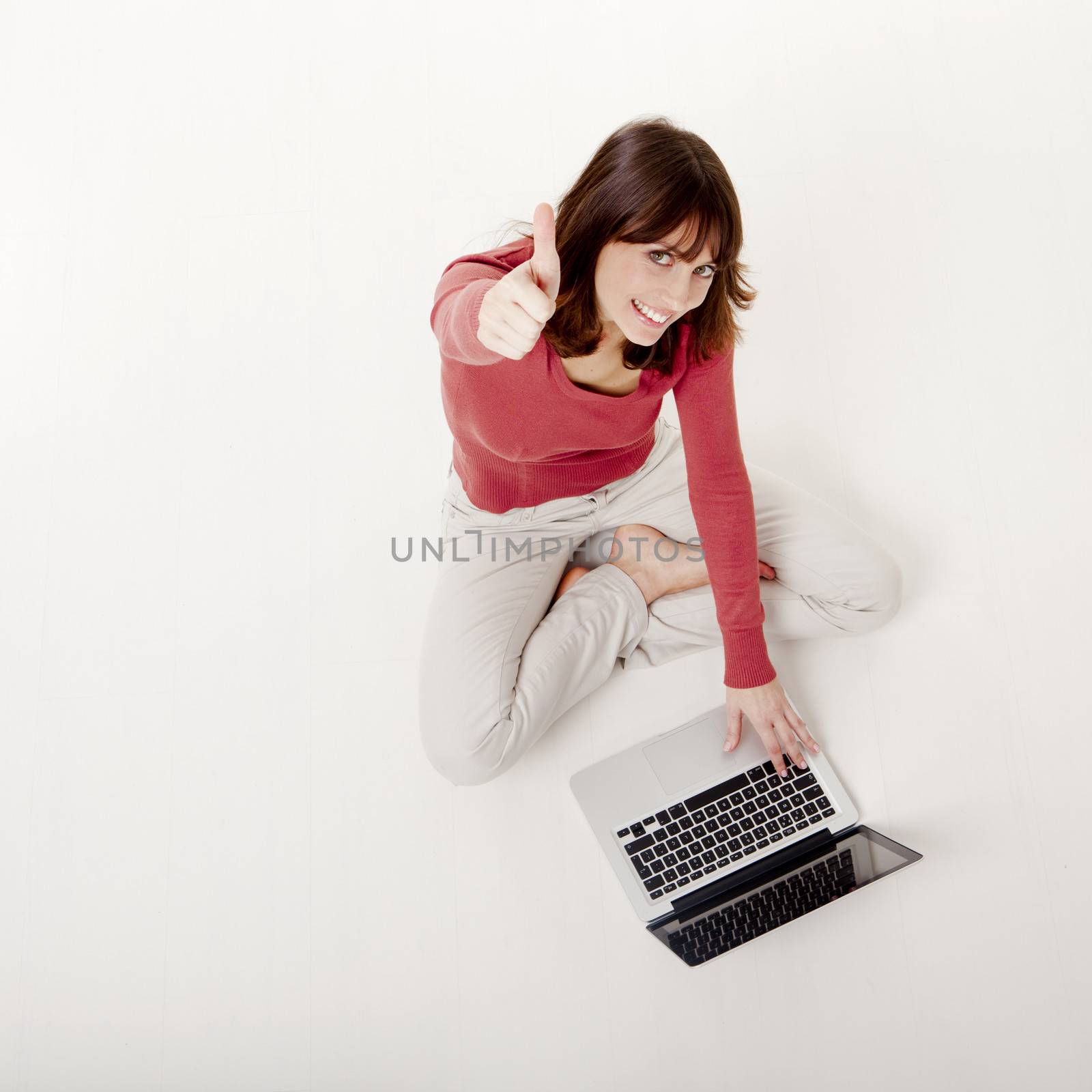 Beautiful happy woman sitting on the floor showing thumbs up, with a laptop