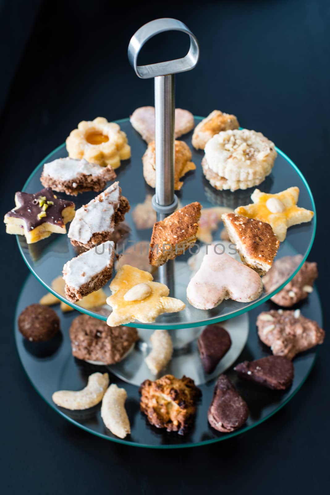 Glass etagere with assortment of cookies on dark wood background