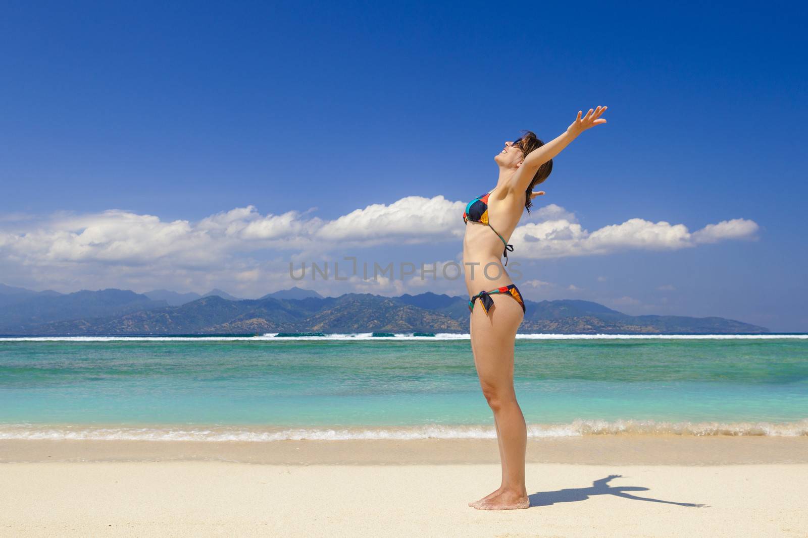 Beautiful woman on a tropical beach with arms open enjoying the summer