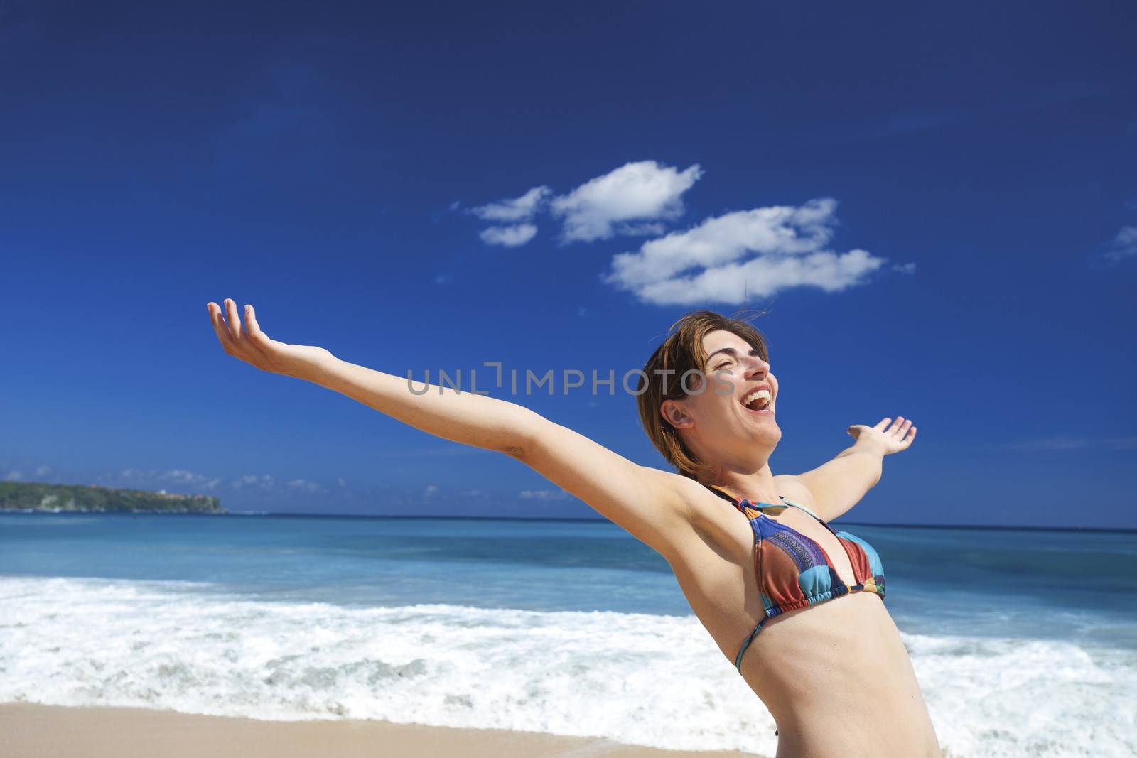 Beautiful young woman with arms open in a tropical beach enjoying the summer 