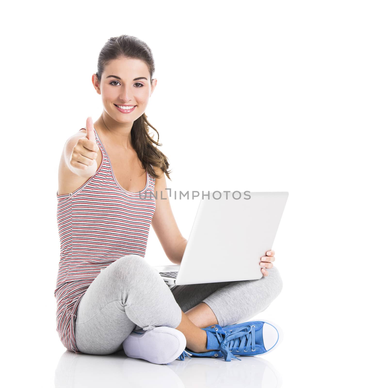 Beautiful student sitting in the floor with a laptop and thumbs up, isolated in white