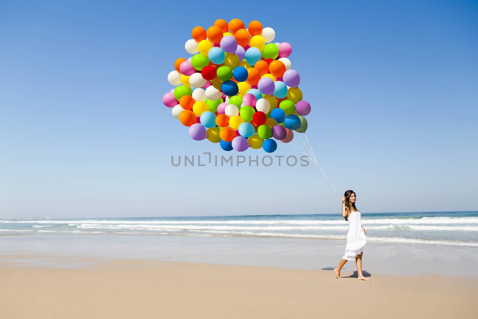 Beautiful girl walking in the beach holding dozens of colored balloons