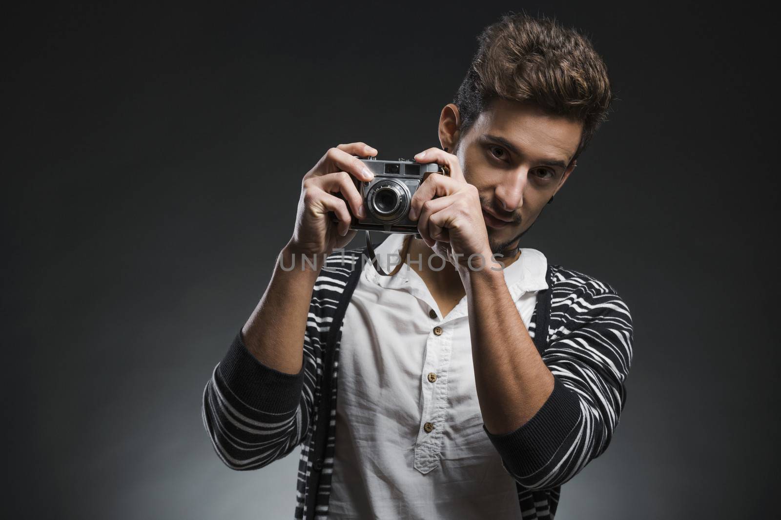 Studio portrait of a fashion young man posing with a old photographic camera, over a dark background