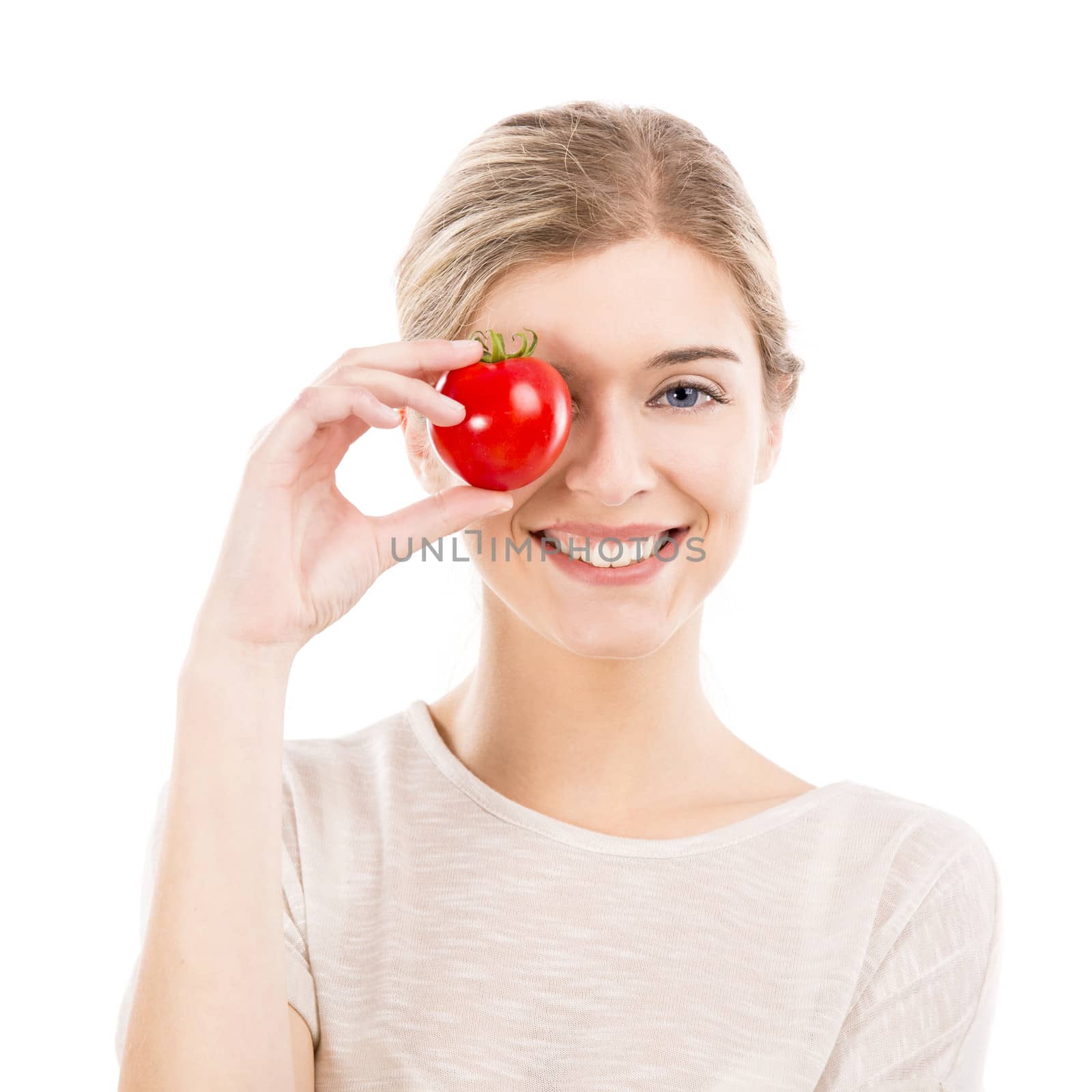 Beautiful girl smiling and holding a red tomato in front of the right eye, isolated over a white background