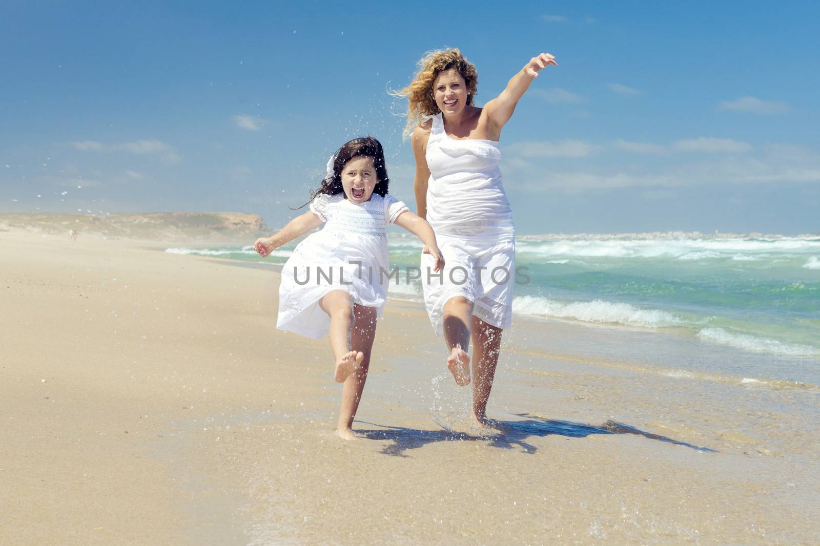 Beautiful pregnant woman and her little daughter really happy playing on the beach