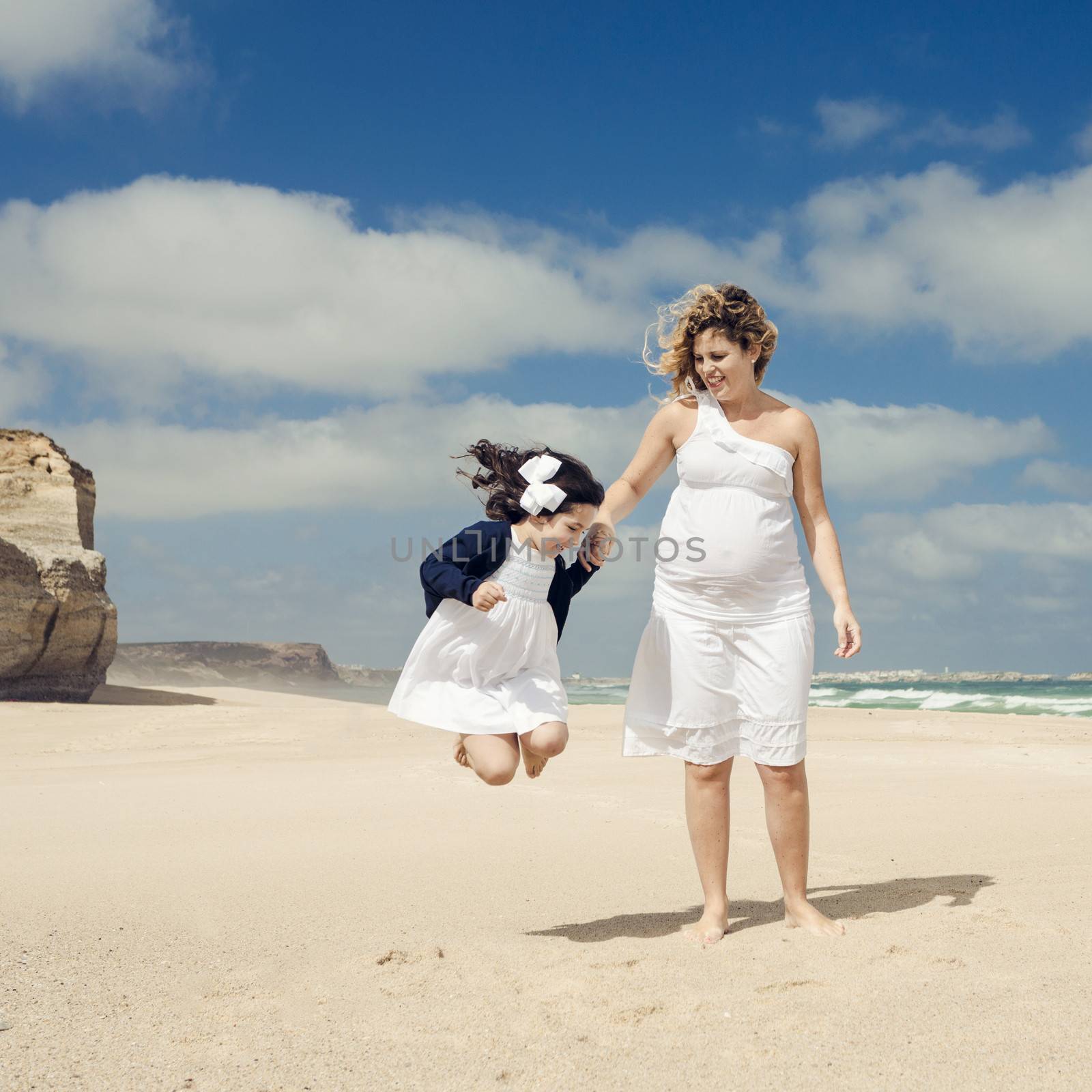 Beautiful pregnant woman and her little daughter playing on the beach