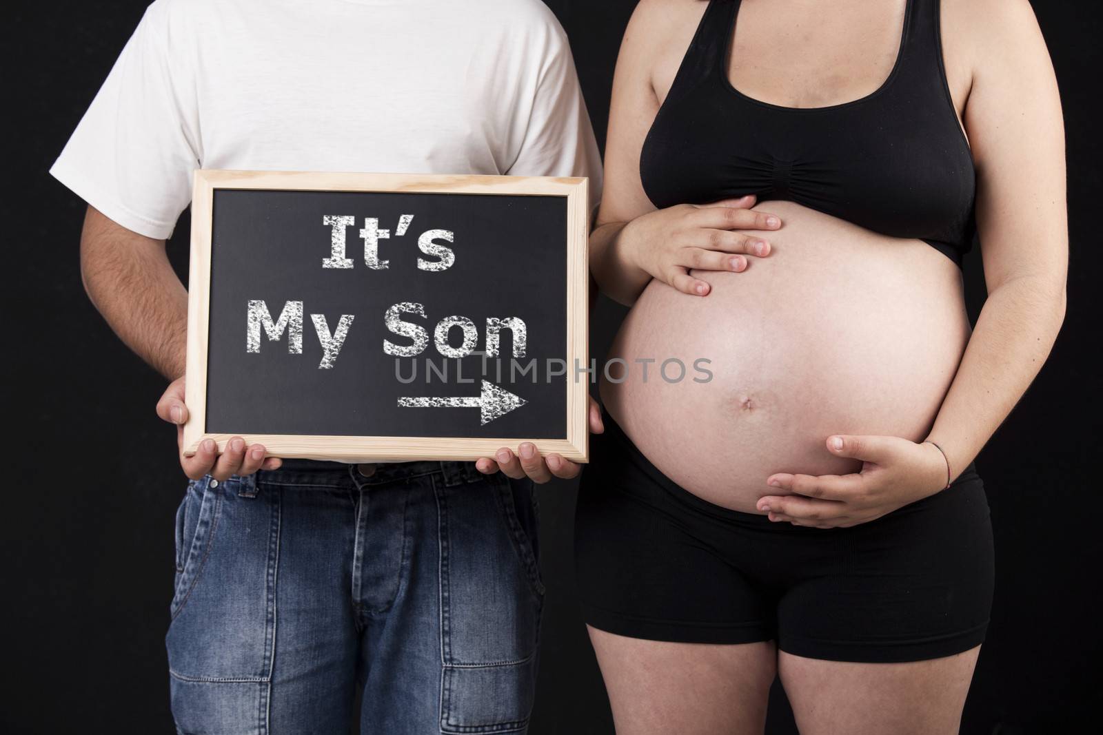Dad holding a chalkboard with the words "It's my Son" and pointing to mom's belly