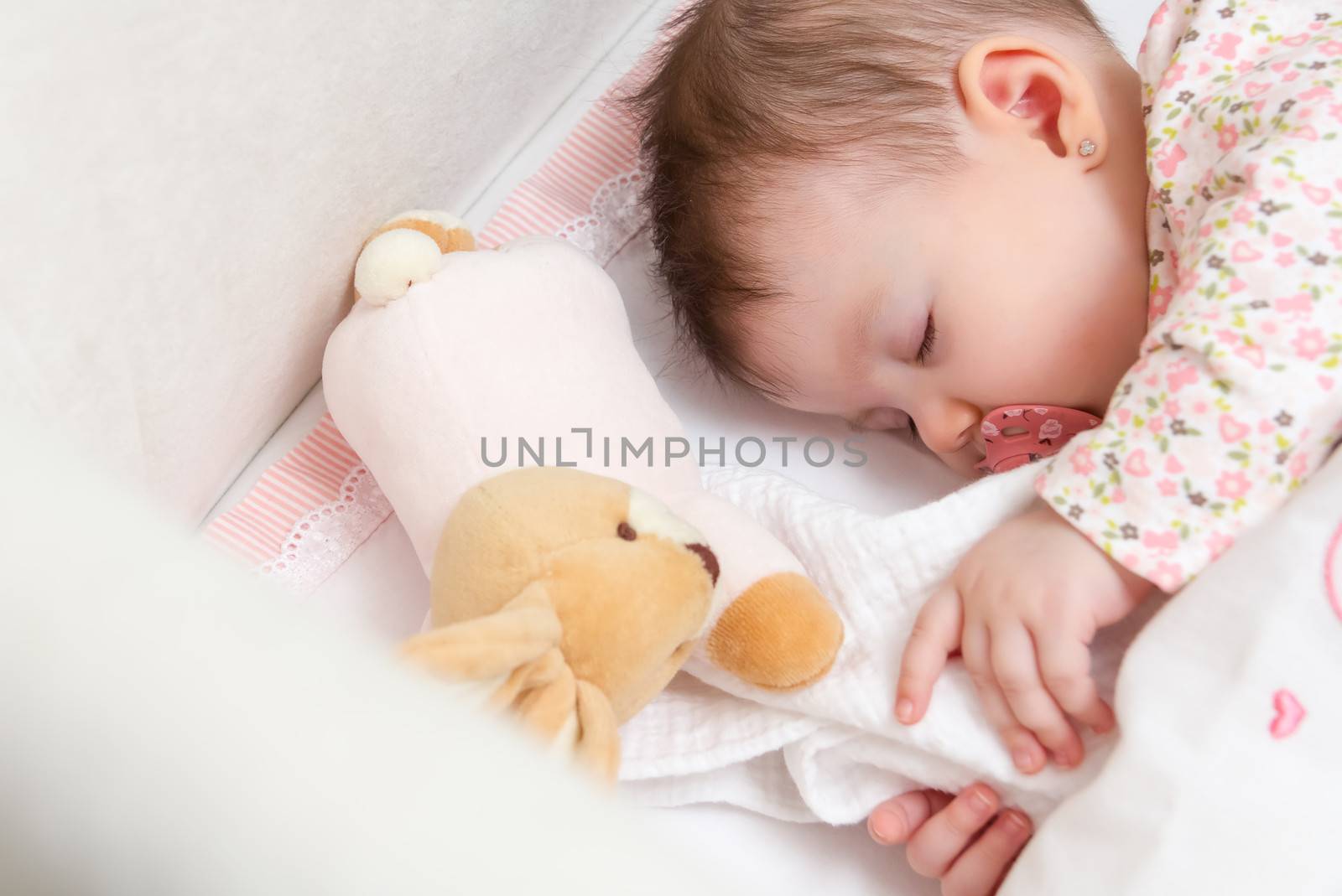 Portrait of cute baby girl sleeping in a cot with pacifier and stuffed toy
