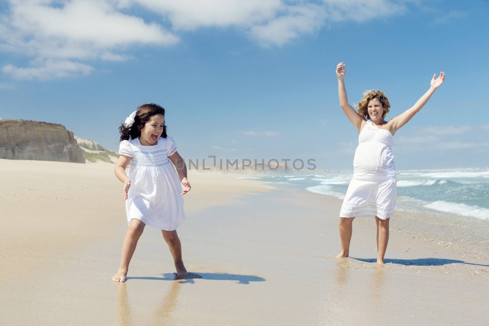 Beautiful pregnant woman and her little daughter really happy playing on the beach