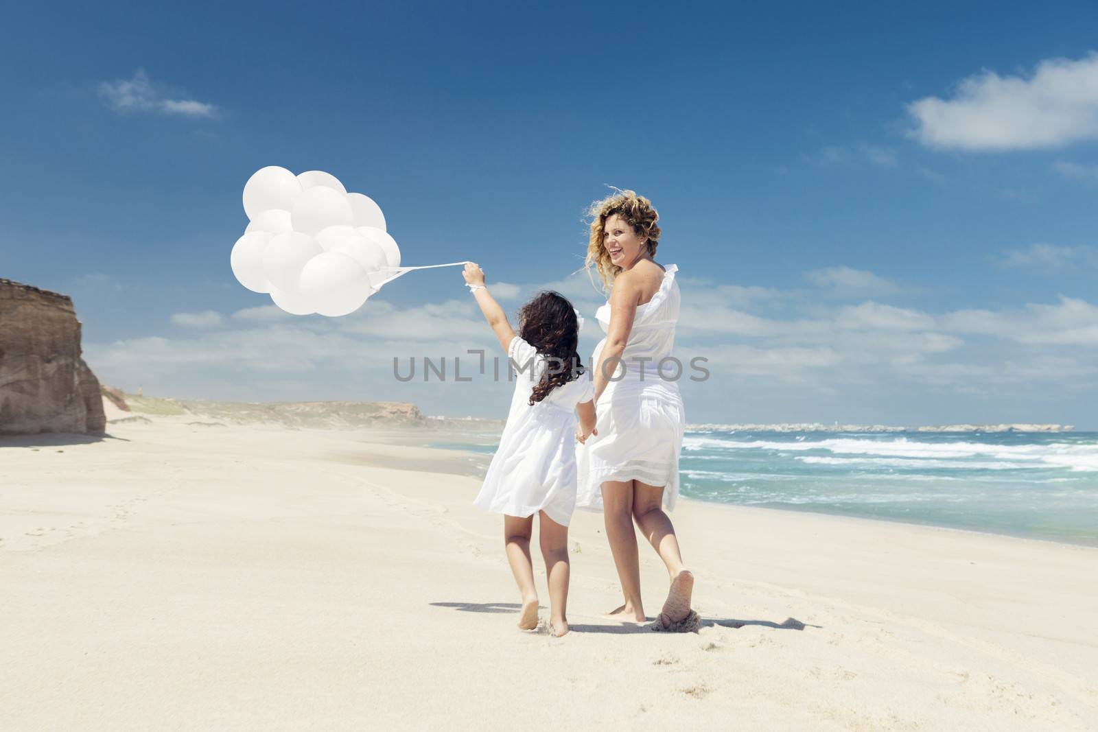 Beautiful pregnant woman and her little daughter walking on the beach with ballons