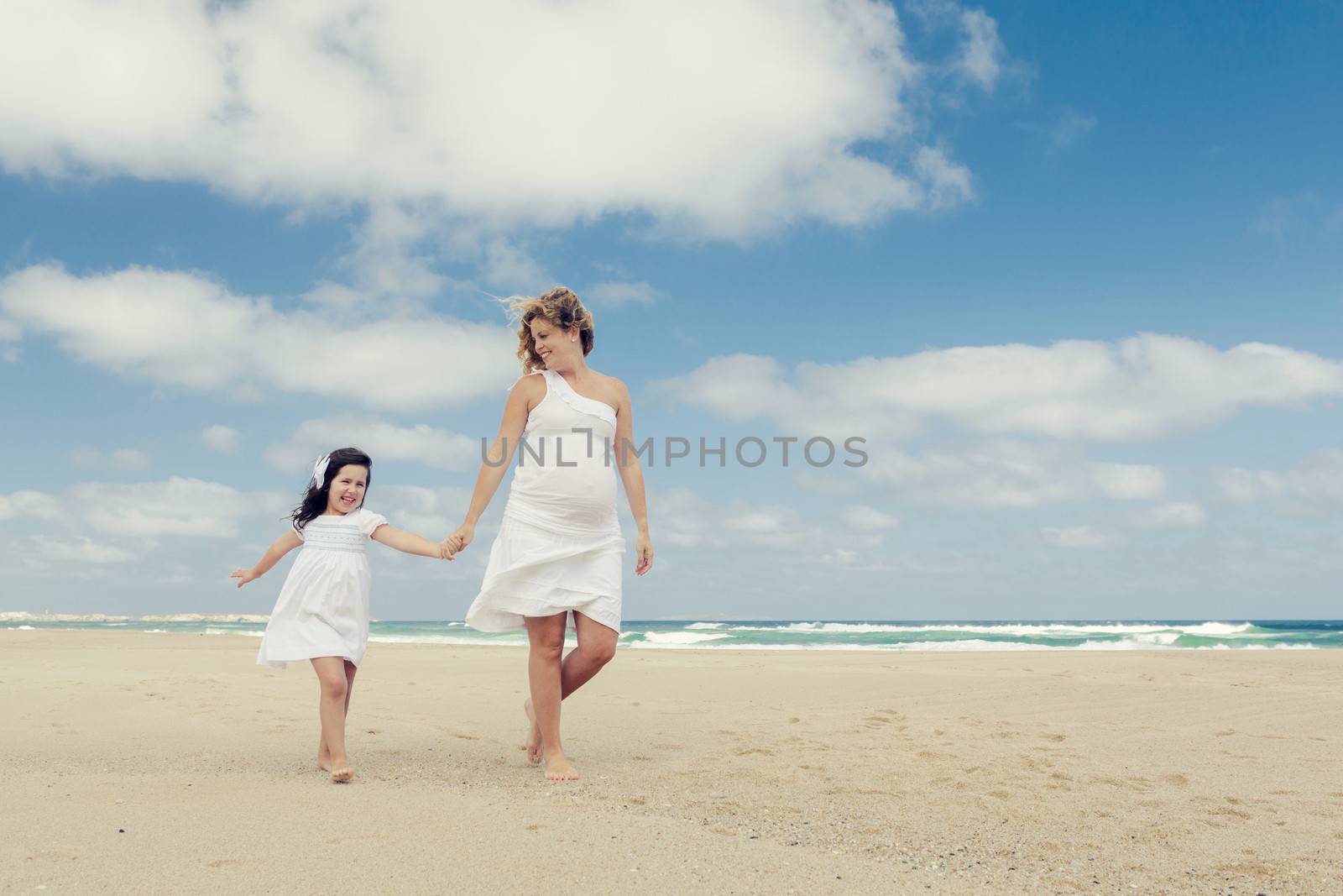 Beautiful pregnant woman and her little daughter walking on the beach