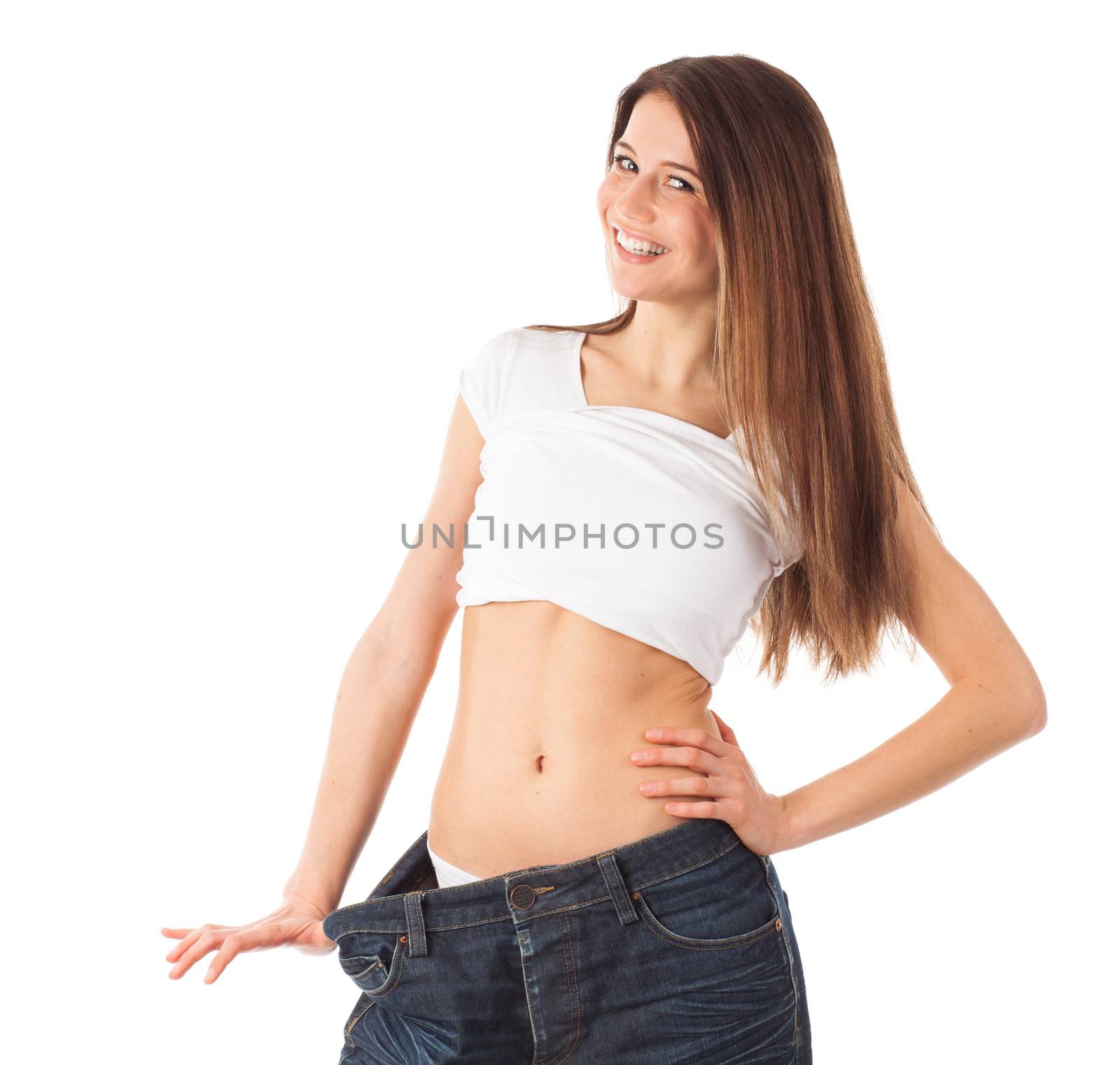 Cheerful young woman showing her waist by wearing an old jeans, isolated on white