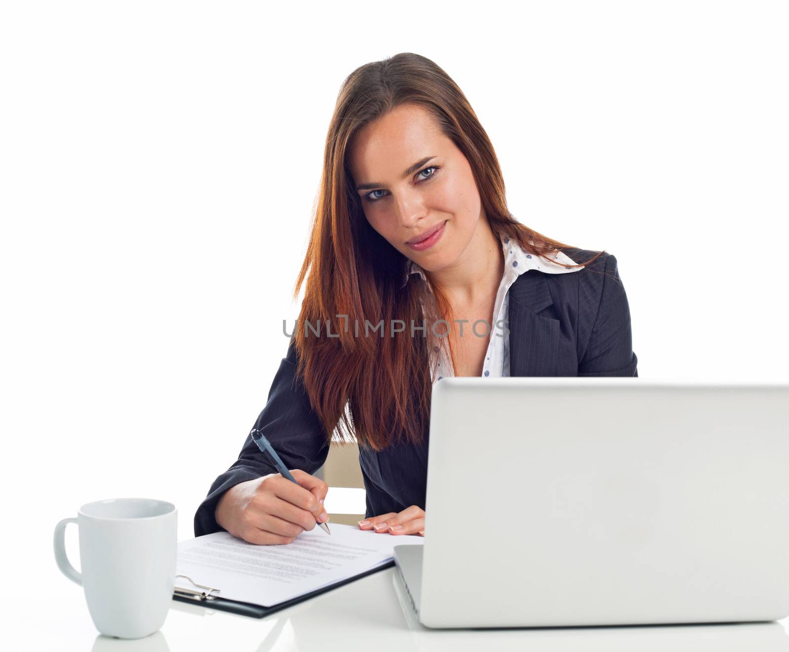 Young business woman working in front a laptop, writing on a paper, isolated on white 