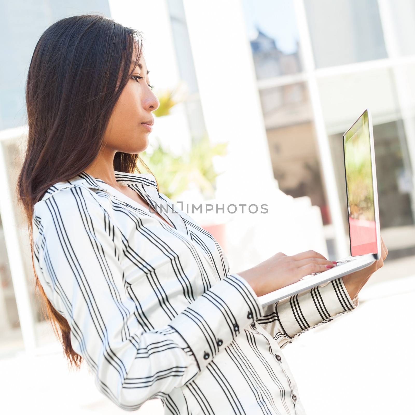 Portrait of a young asian woman standing using a laptop