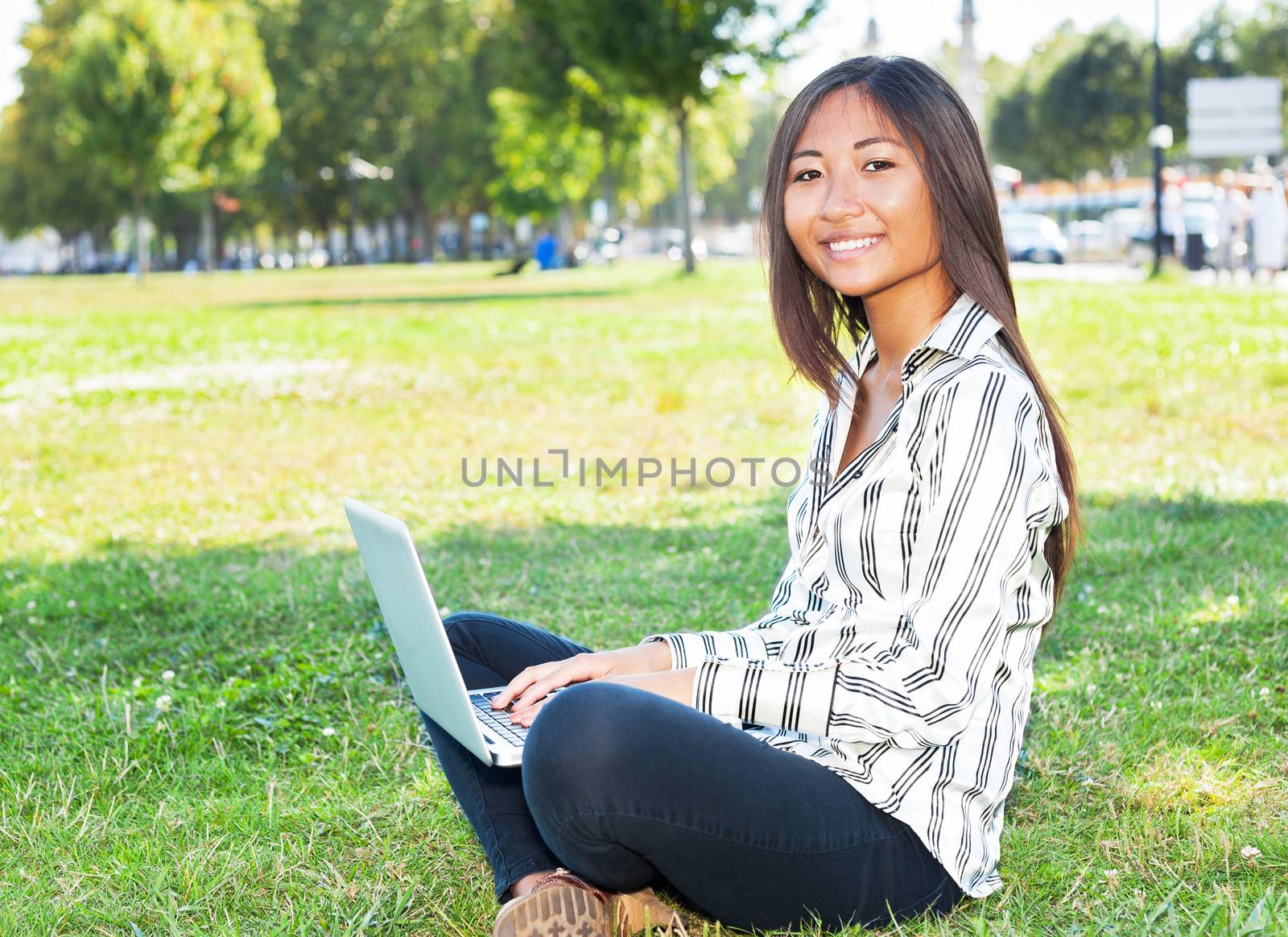 Asian woman writing on a laptop in a park by TristanBM