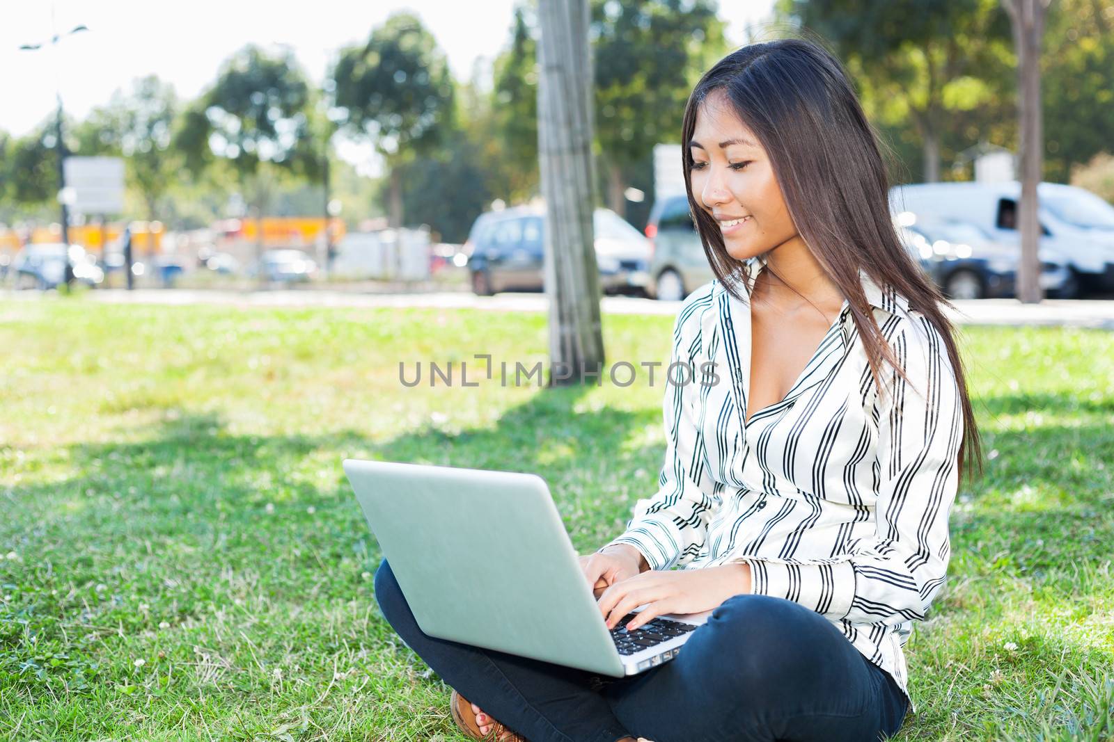 Smiling asian girl using a laptop sitting on the grass