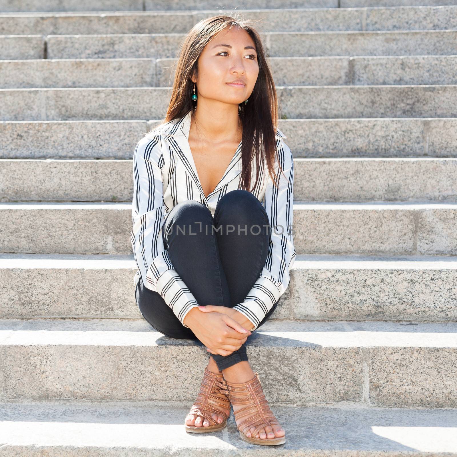 Portrait of a pretty asian woman sitting on stairs outdoors and looking something