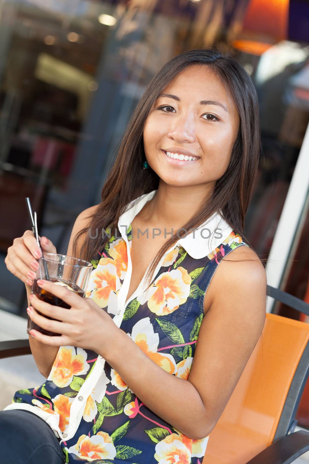 Portrait of a smiling asian girl drinking a soda sitting on terrace