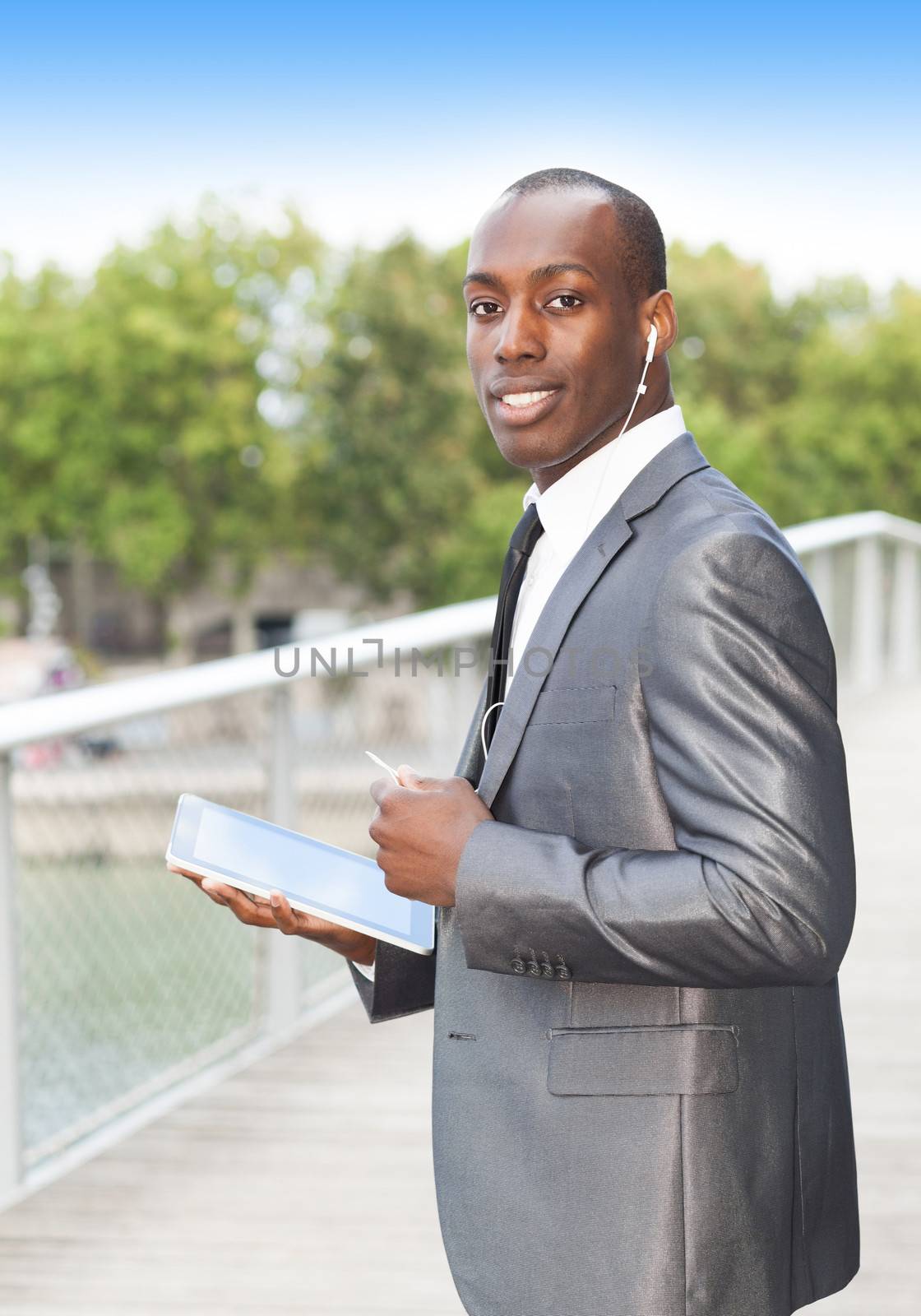 Portrait of a smiling businessman on the phone with hands-free headset and using electronic tablet