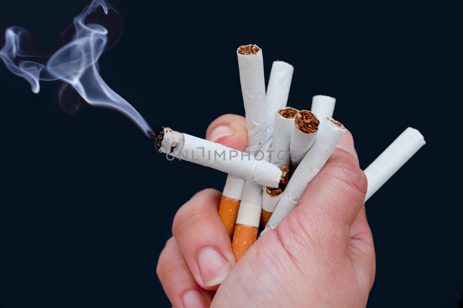 Hand squeezing many cigarettes including one lit up  