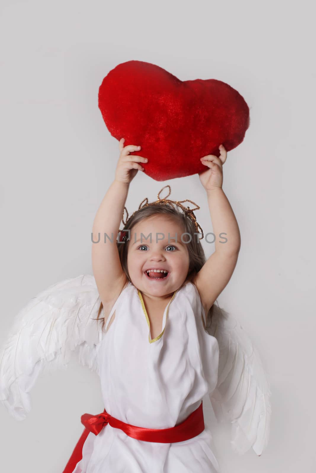 Joyful cupid girl holds plush heart over head isolated onmwhite