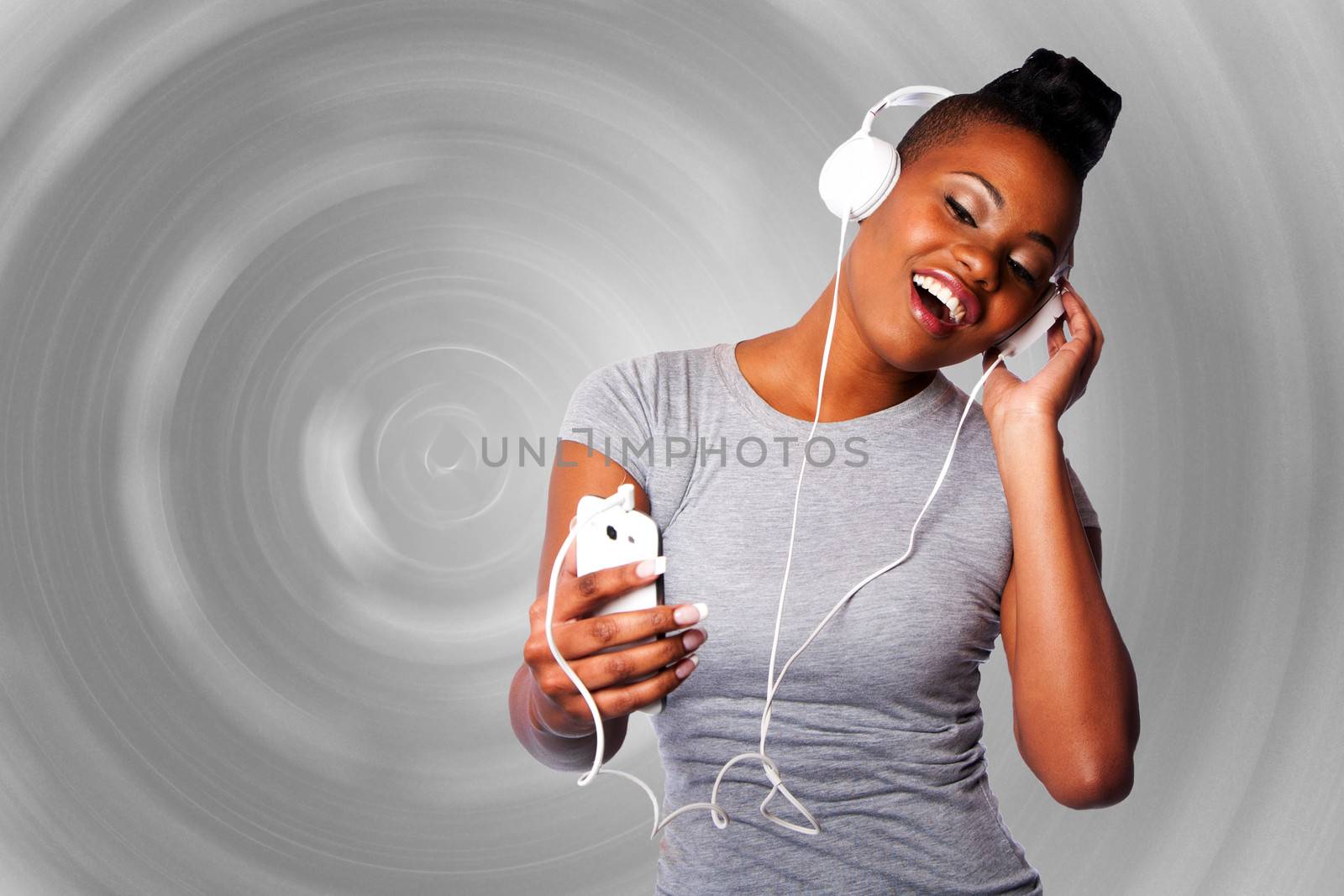 Beautiful young woman with headphones and mobile device listening grooving singing to music, gray circular background.
