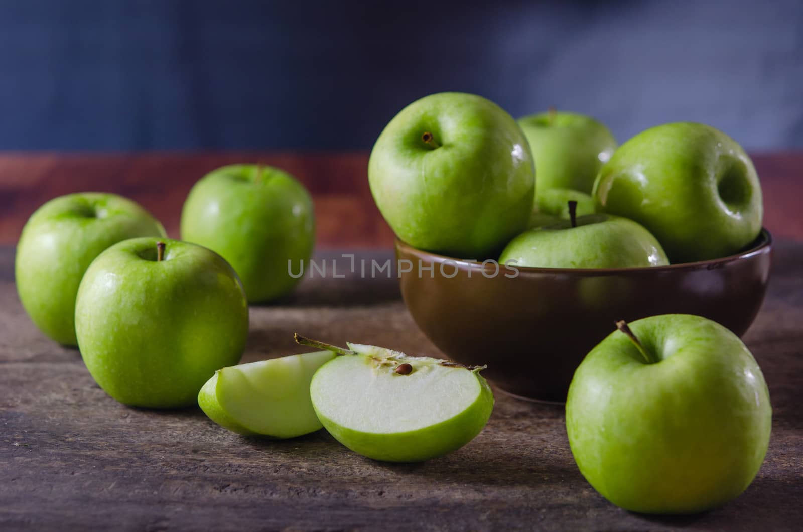 Bowl of green apples and slices of apple over wooden board