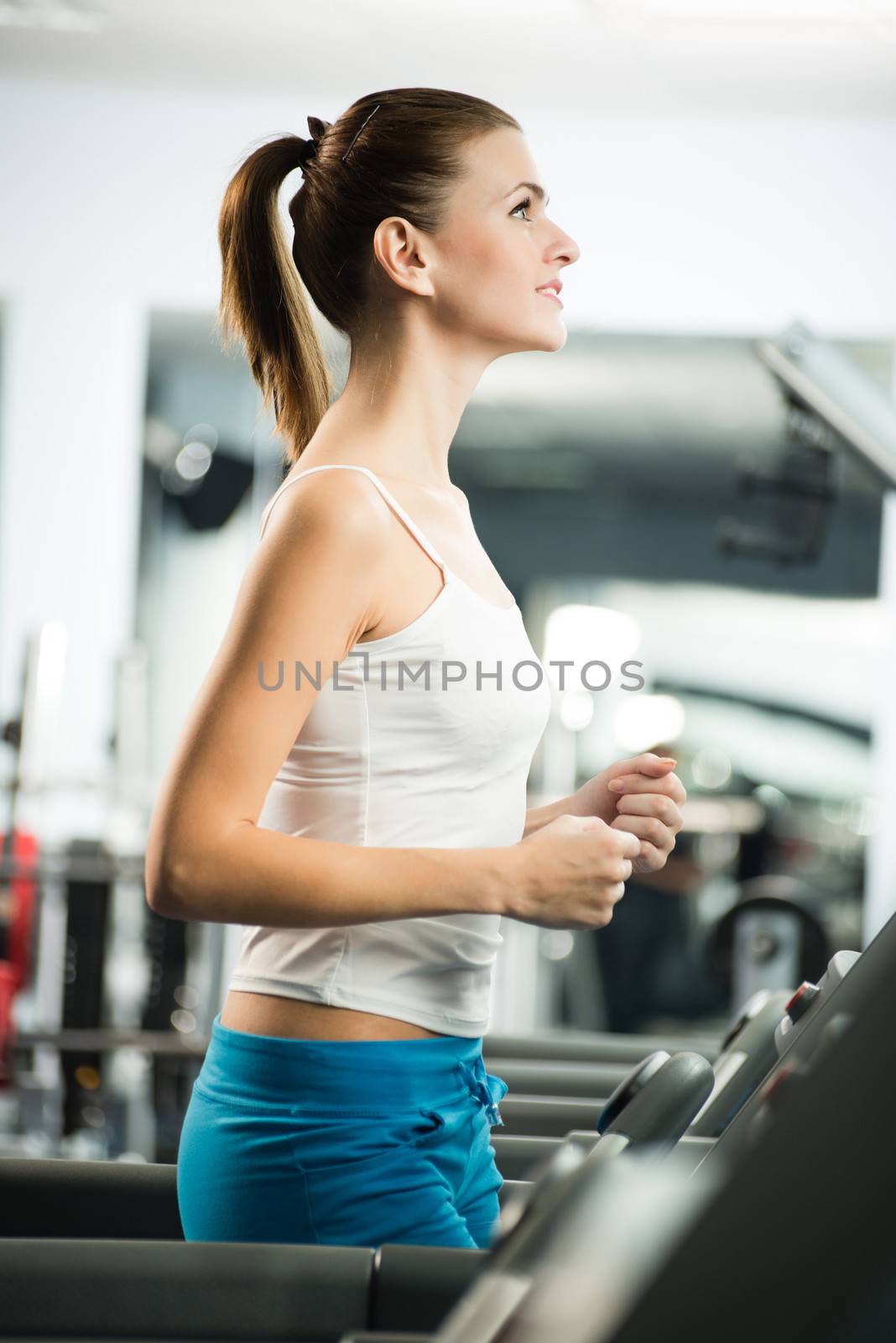 attractive young woman runs on a treadmill by adam121
