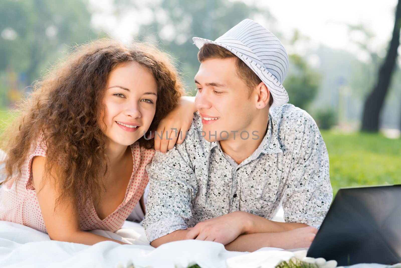 couple lying together in a park, working together on a laptop