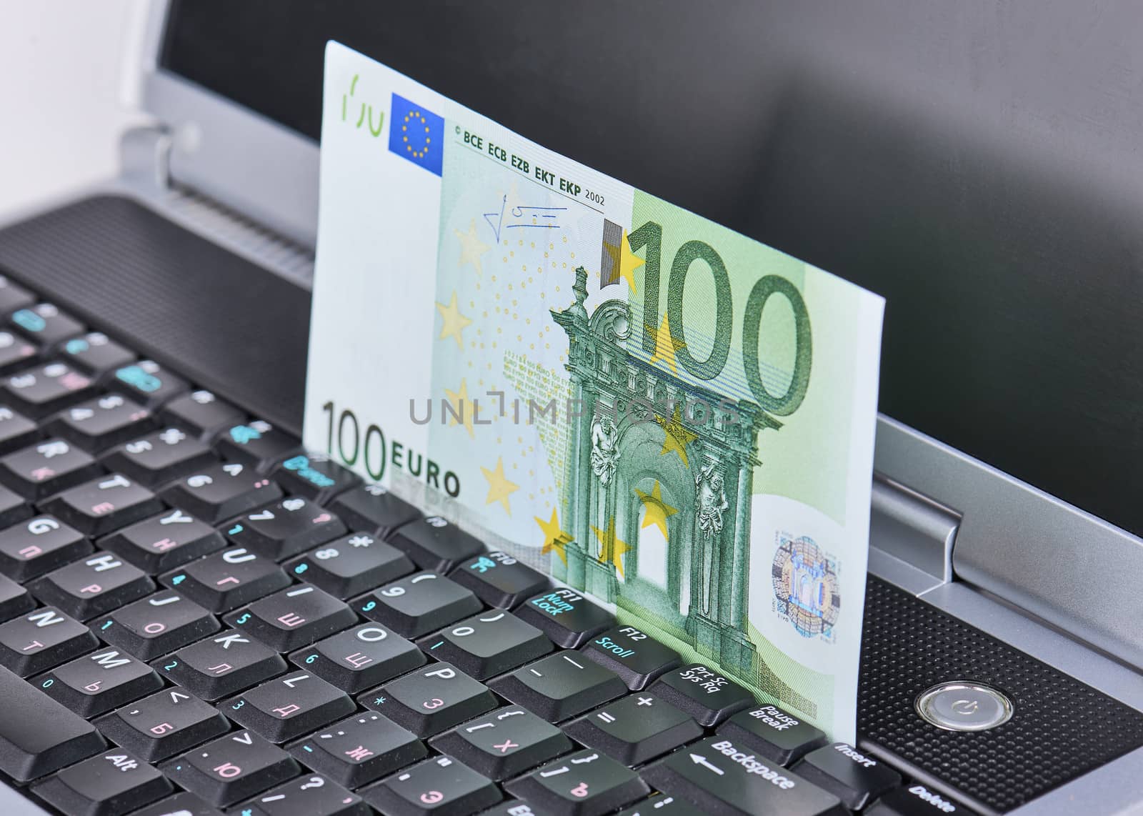 100 euro banknote displayed in motion on a laptop keyboard closeup.