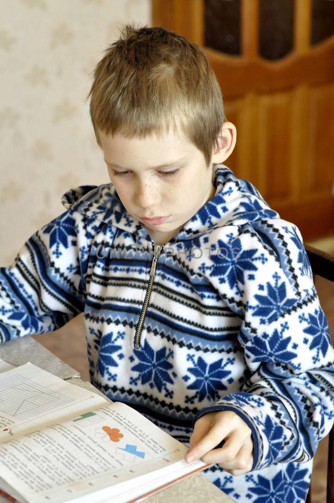 The 10-year-old boy sits with the textbook, doing homework