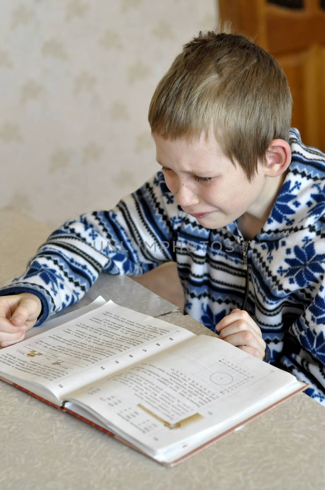 The 10-year-old boy with tears in the eyes sits before the textbook, doing homework