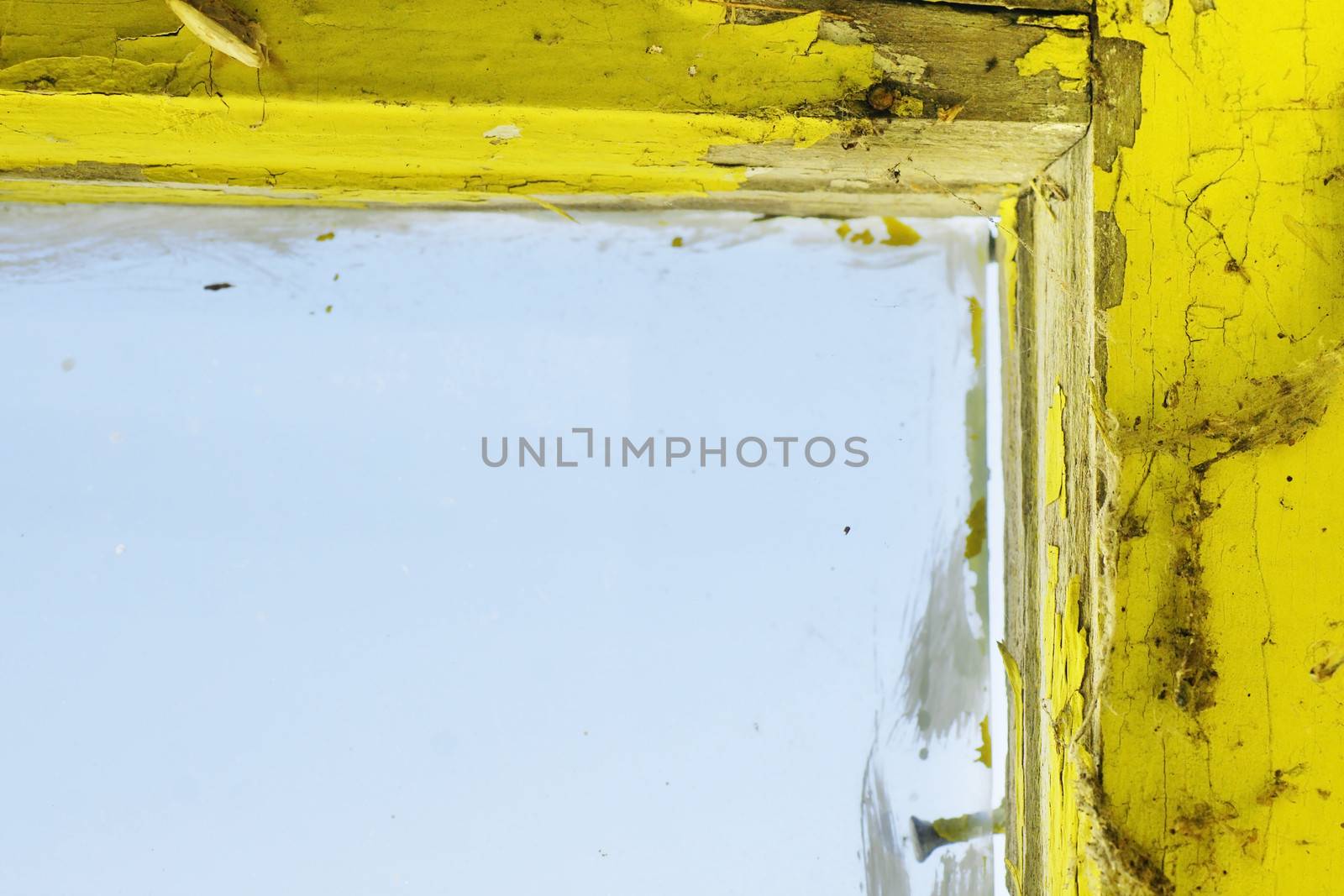 Old and dirty yellow painted wooden window frame and glass, with cobweb