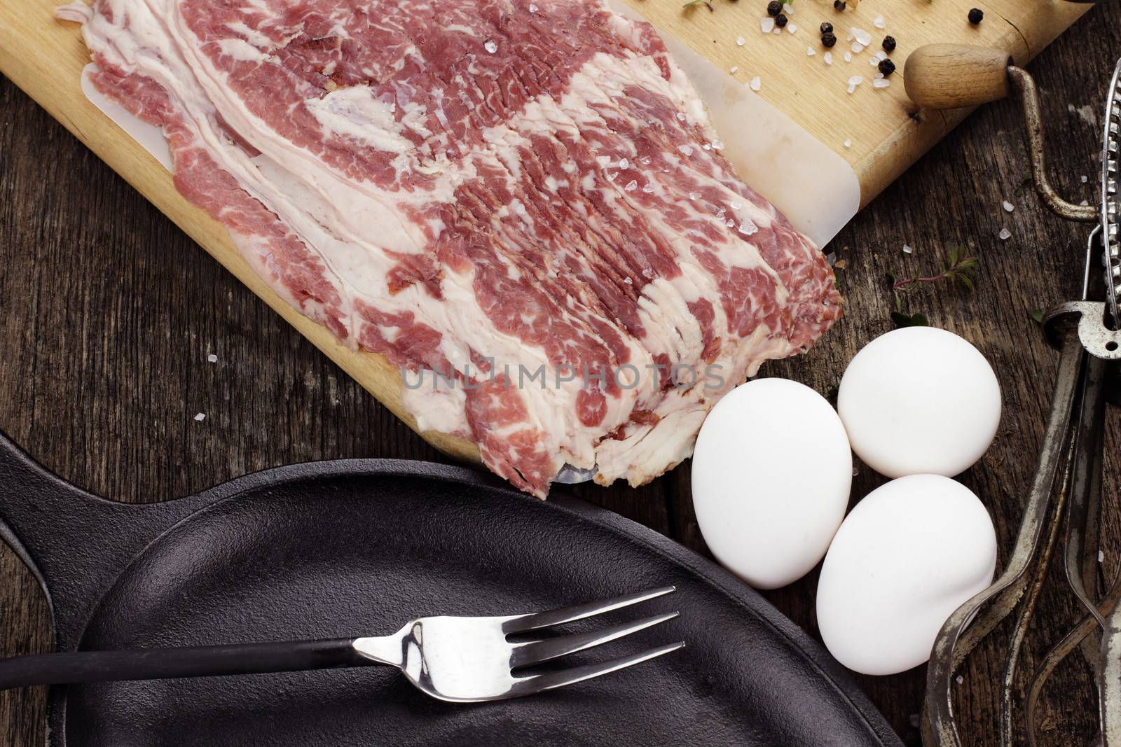 Breakfast ingredients, cast iron skillet and uncooked beef bacon with fresh eggs and herbs. 