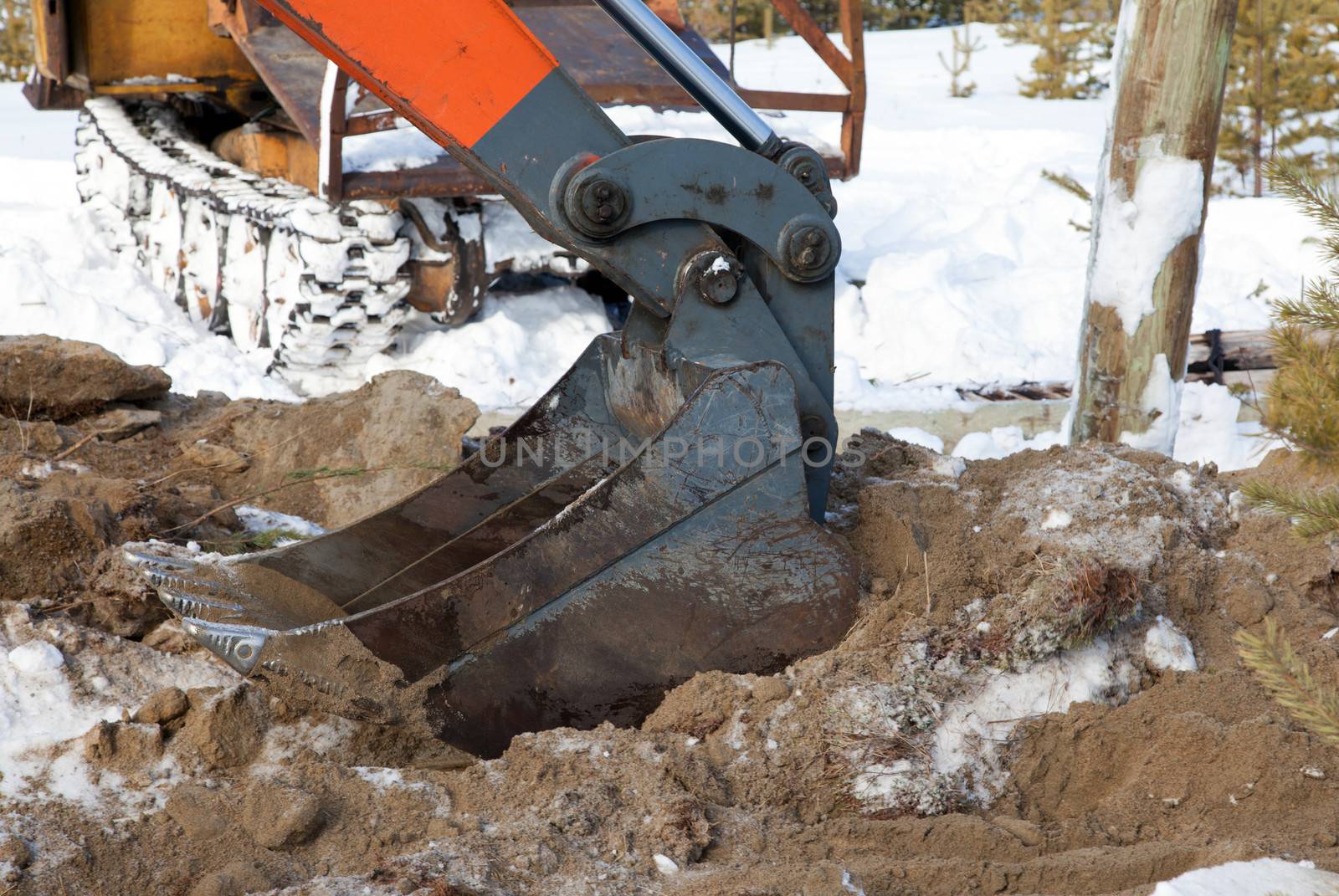 
Bucket hydraulic excavator digging a pit in a snowy forest 
