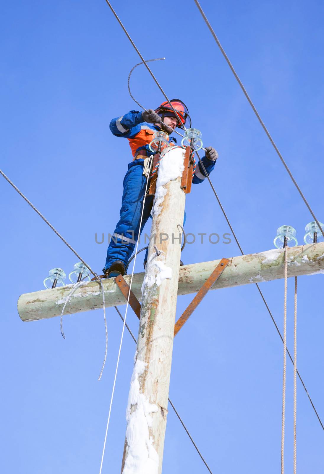 electrician working on top of an electricity pylon with the use of claws-manholes and belt 