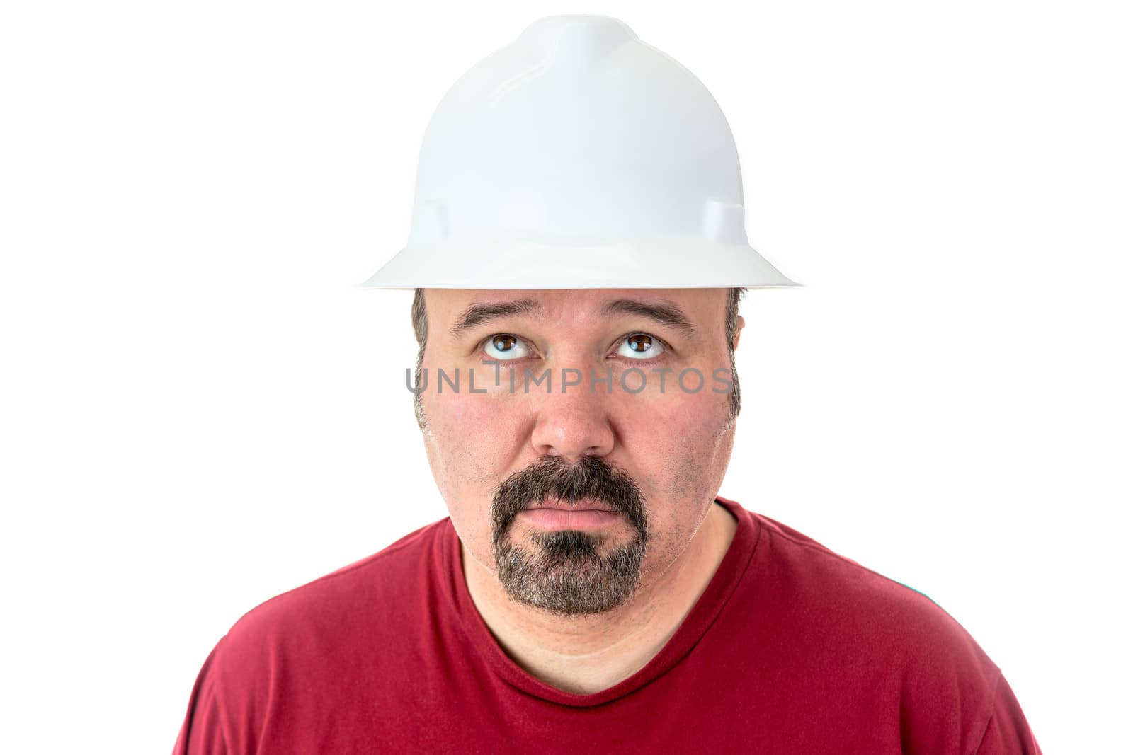 Glum looking workman wearing a hardhat looking for inspiration raising his eyes to the heavens in supplication, isolated on white