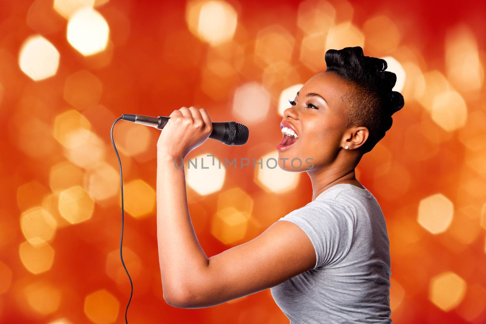 Beautiful teenager woman singing kareoke concert artist holding microphone, on red orange blurred lights background.